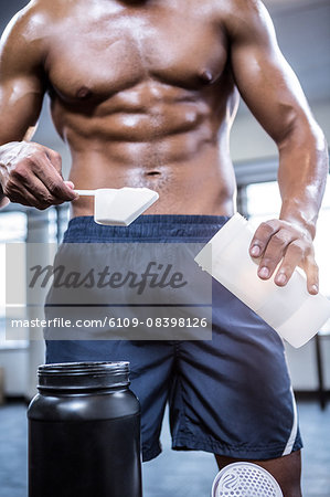 Fit shirtless man scooping protein powder
