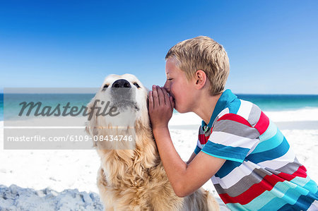 Cute boy whispering a secret to his dog on the beach