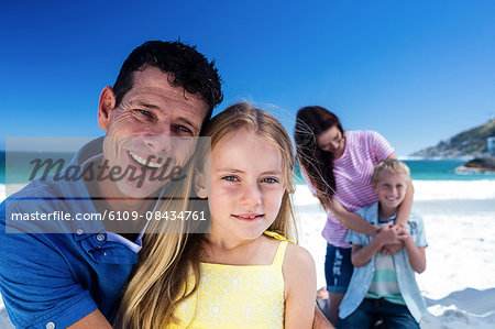 Cute family smiling with arms around on the beach
