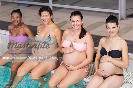 Smiling pregnant women touching their belly at the swimming pool