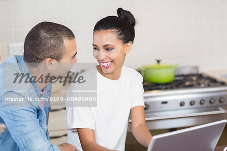 Young couple using laptop together in the kitchen at home