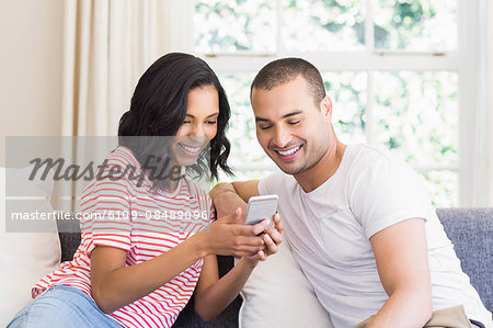 Happy couple using smartphone on the couch at home