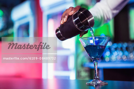 Bartender pouring cocktail from shaker into glass at bar counter in bar