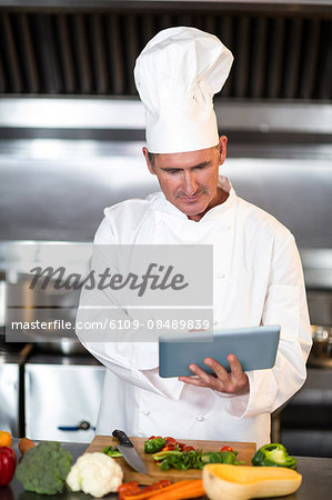 Chef preparing vegetables at counter with tablet in a commercial kitchen