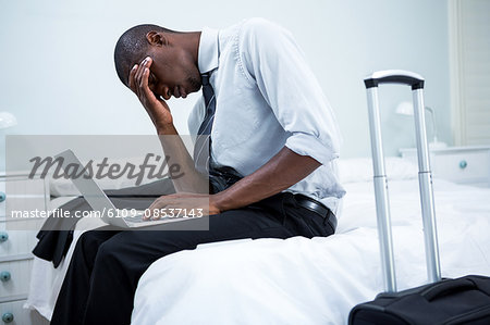 Tensed man sitting on bed and using laptop