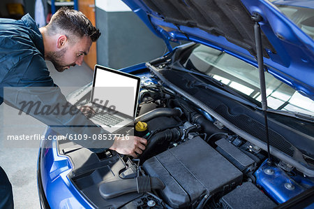 Mechanic examining car engine with help of laptop