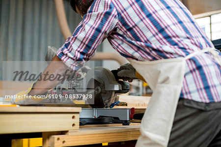 Carpenter cutting wooden plank with electric saw