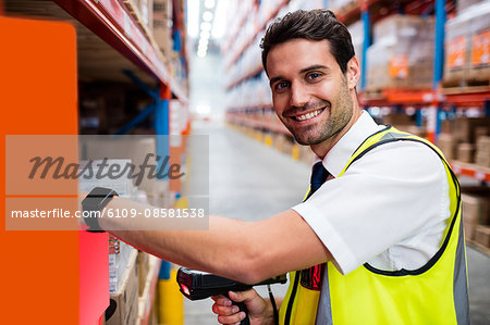 Smiling warehouse manager with yellow coat scanning barcode on box