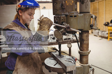 Female welder using a drill press in a workshop