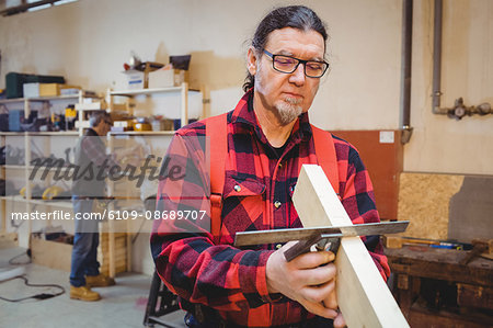 Carpenter looking if the wood plank is straight in his workshop