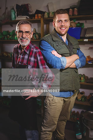 Duo of cobblers with arms crossed posing in their workshop