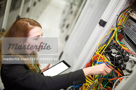 Technician holding digital tablet while examining server in server room