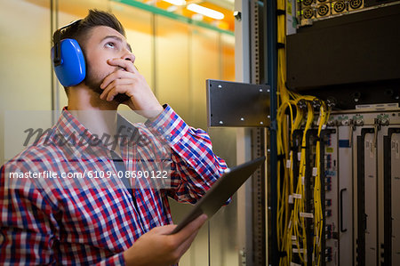 Technician in head phones using digital tablet while analyzing server in server room Technician in head phones using digital tablet while analyzing server in server room