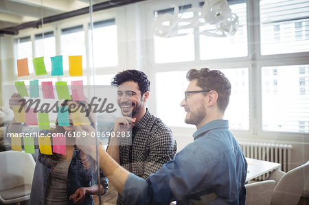 Cheerful creative business people looking at sticking notes on glass in office Cheerful creative business people looking at sticking notes on glass in office