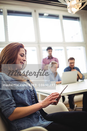 Smiling businesswoman using digital tablet against coworkers in meeting room at creative ofice