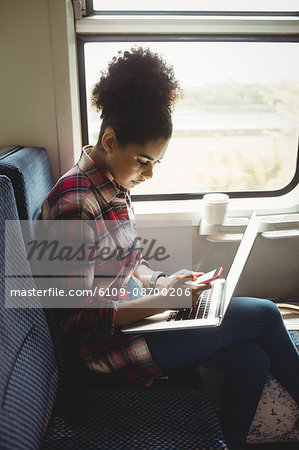 Side view of woman using phone with laptop while sitting in train