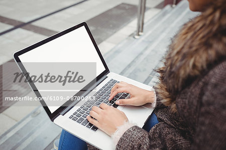 Cropped image of woman typing on laptop while sitting on steps