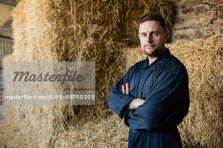 Portrait of confident farm worker standing against hay bales in barn