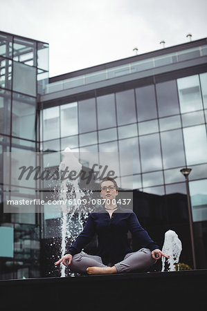 Full length of businesswoman in lotus position against office building