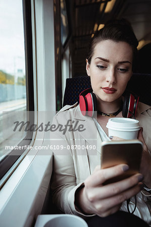 Pretty woman using mobile phone while sitting by window in train