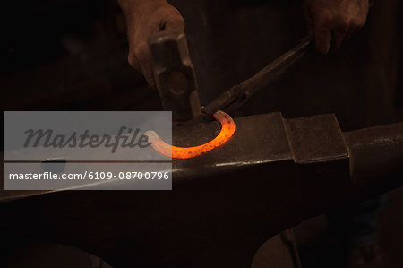 Hands of blacksmith working on a metal piece with hammer in workshop