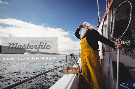 Fisherman holding fishing net and looking at view from boat