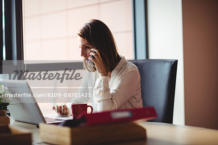 Woman using laptop and talking on mobile phone in the office