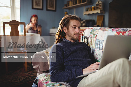 Hipster man using laptop while woman sitting in background at home