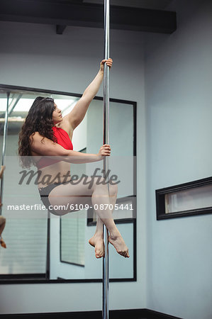 Pole dancer practicing pole dance in fitness studio