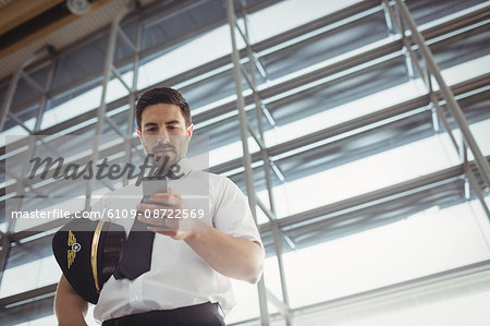 Pilot using mobile phone in waiting area at airport terminal