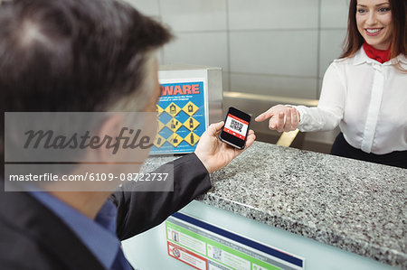 Businessman showing mobile boarding pass to airline check-in attendant at check-in counter