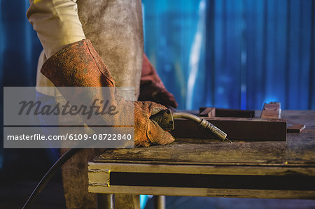 Mid-section of male welder holding welding torch in workshop