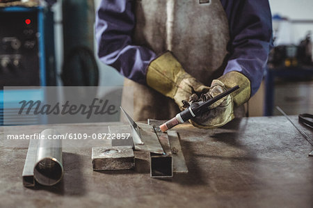 Mid-section of female welder working on a piece of metal in workshop