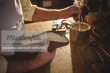 Shoemaker applying glue on shoe sole in workshop