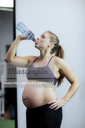 Pregnant woman drinking water during break in gym