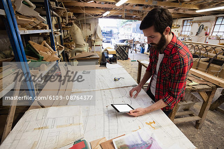 Man using digital tablet while looking at blueprint in boatyard
