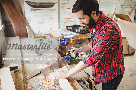 Man cutting a wooden plank at boatyard