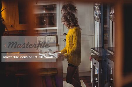 Beautiful woman using digital tablet while having coffee in kitchen at home