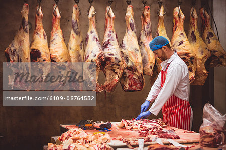 Butcher chopping meat in storage room at butchers shop
