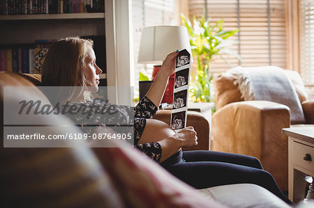 Pregnant woman looking at a sonography in living room at home