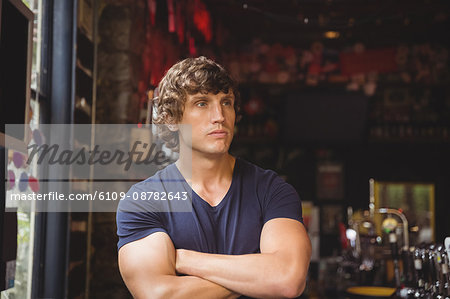 Bar tender standing with arms crossed at bar counter