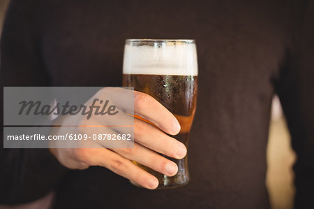 Mid section of man holding glass of beer at bar
