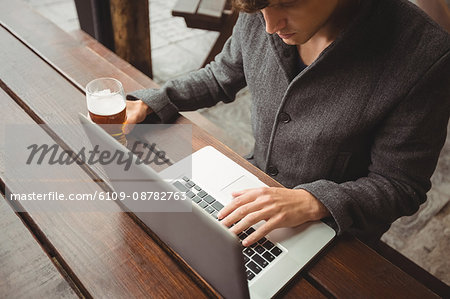 Man using laptop while having glass of beer in bar