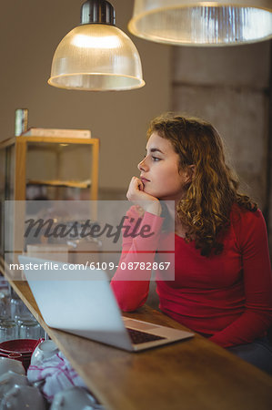 Thoughtful woman sitting at counter with laptop in bicycle shop