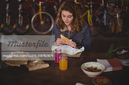 Woman sitting at table and eating sandwich in bicycle shop