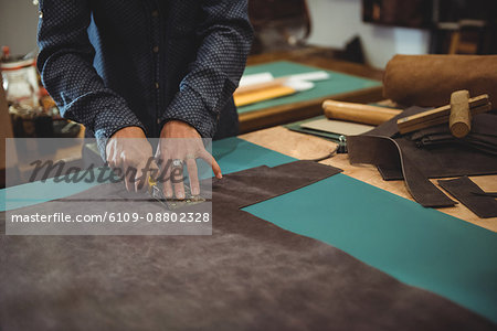 Mid-section of craftswoman cutting leather in workshop
