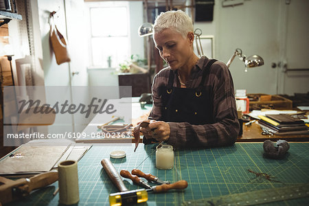 Attentive craftswoman preparing leather belt in workshop