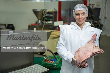 Portrait of female butcher holding meat at meat factory