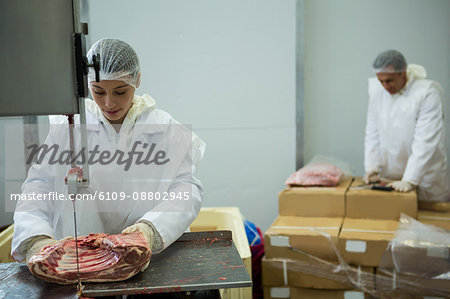 Portrait Of A Female Butcher Cutting A Piece Of Meat In Butchers