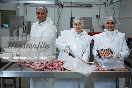Portrait of butchers packing sausages at meat factory